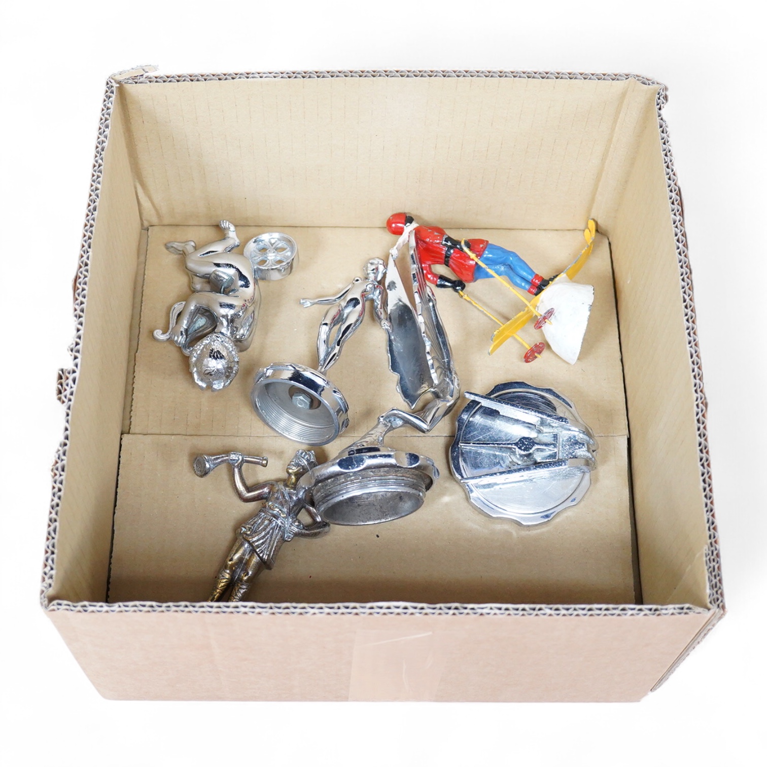 Six car mascots including five chrome and brass examples; a female figure, a cherub with harp, an Art Deco winged figure, etc. and a cold painted spelter figure of a skier